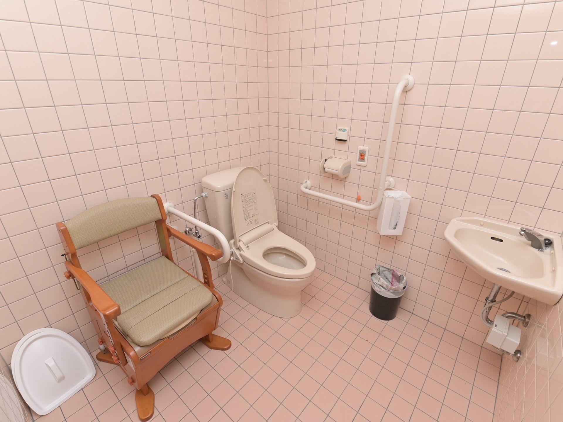 タイル張りのトイレ空間に、洋式便器と、椅子型の便器が設置されている。手すりのそばにナースコールがついていて安心である。