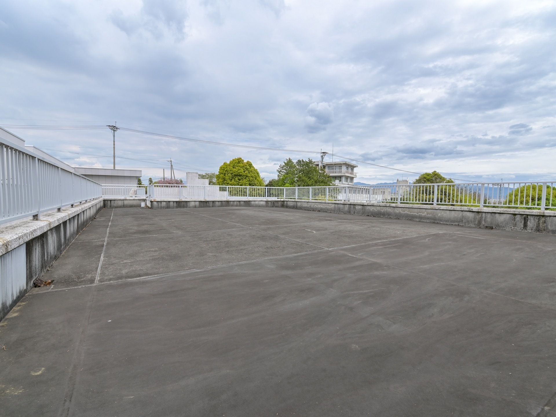 建物の屋上部分は平らに広がっていて、四方が柵で囲まれている。周囲のやまなみや庭木が茂る様子が見える。