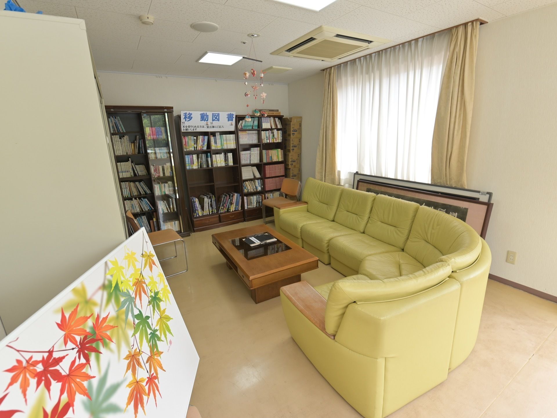 部屋の中央に黄緑色のソファーが据えてある。奧の壁面には、背の高い本棚があり、複数の書物が納められている。