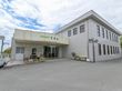 玄関の屋根部分に、施設名称表示が施されている。建物の前に、椅子やテーブル、プランターなどが配置してある。