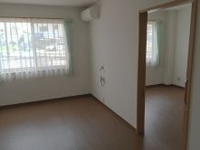 エアコンが設置されたフローリングの部屋にはレースカーテンとカーテンが付いた窓があり、二間続きとなっている。