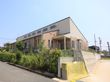 薄い茶色とベージュの外壁をした建物がある。前の道路は坂道になっていて、敷地はコンクリートで底上げされている。