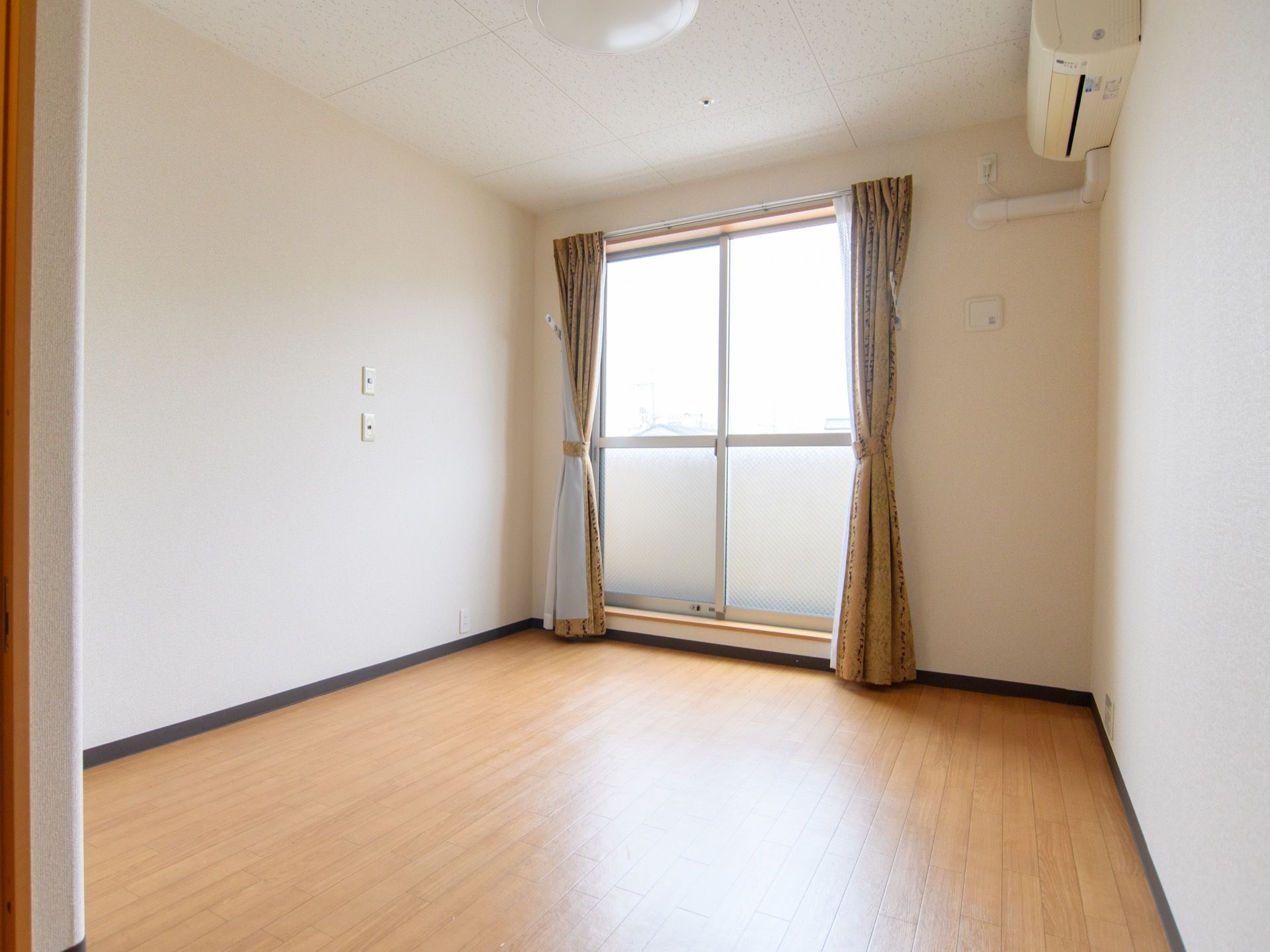 居室には大きな窓を設け、日差しを調整するダブルカーテンを掛けている。壁にはエアコンを一台設置している。