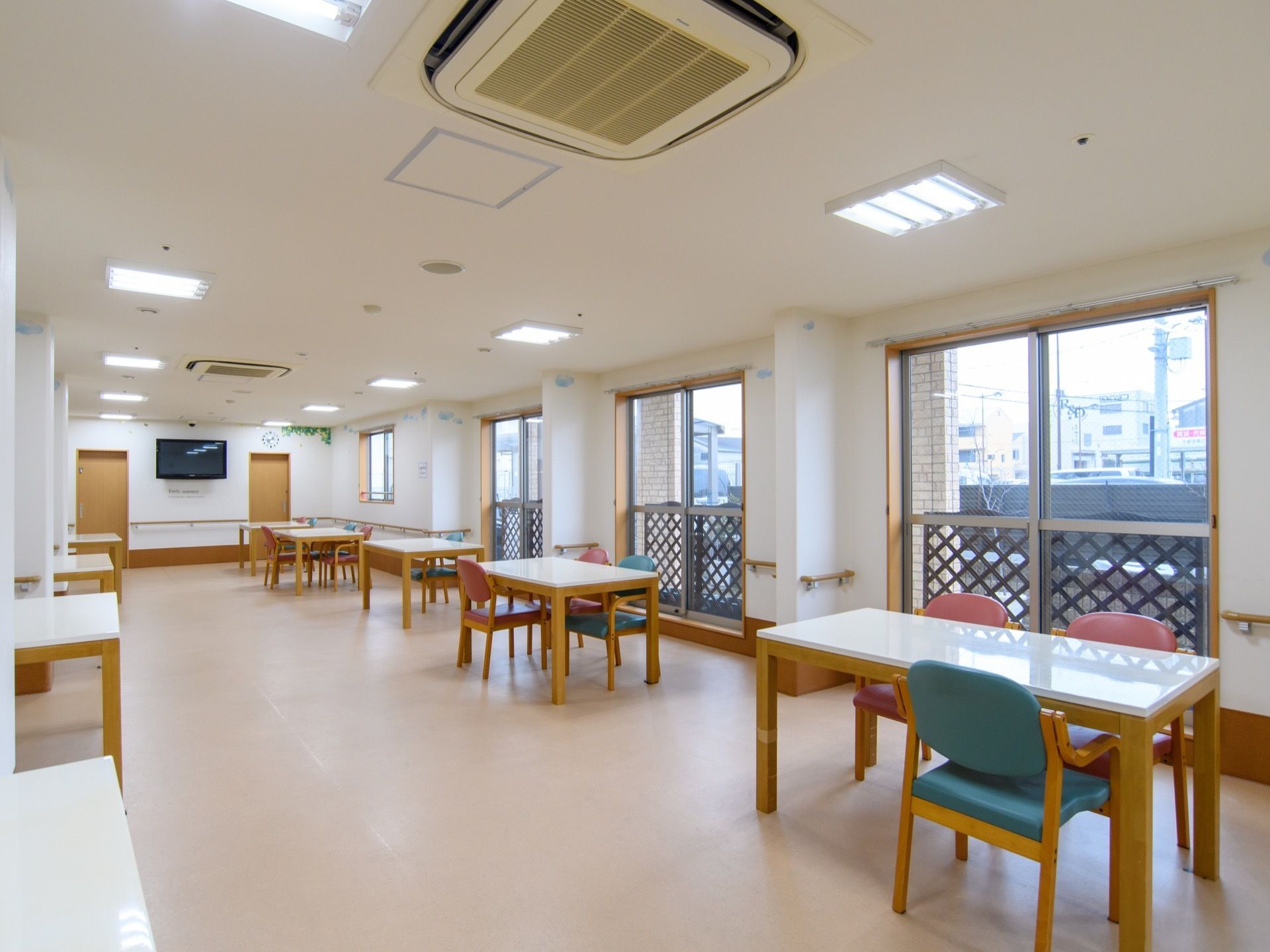 食堂には大きな窓があるので日当たりが良い。壁には液晶テレビを設置し、その下には手すりを取り付けている。