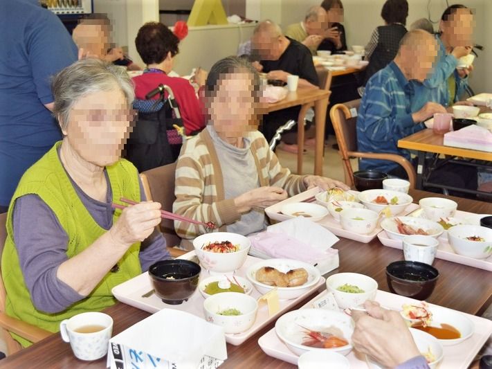 施設内で食事をとる高齢者の様子。おかずやご飯が乗ったトレーがある