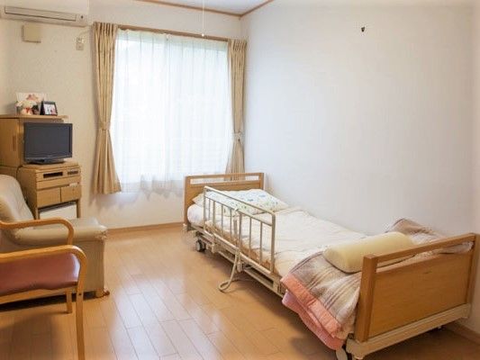 エアコンが付いたフローリングの居室。一人用のソファやテレビ、寝具付きのベッドがある。