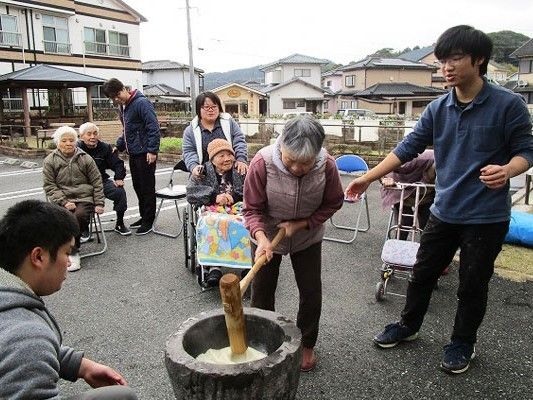 敷地内の駐車場の一角でもちつきを楽しむ入居者とスタッフ。椅子に座って見物をしている入居者もいる。