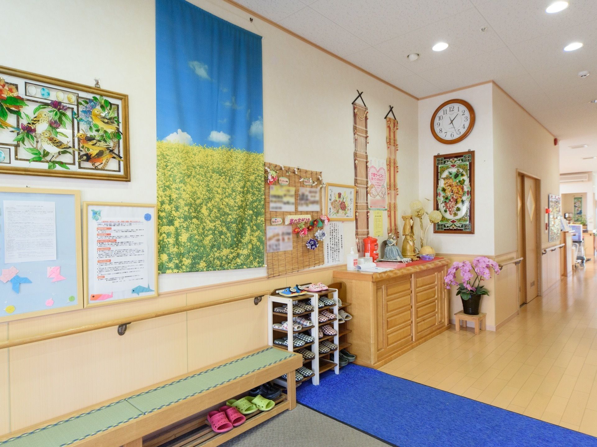 玄関脇の壁には、お知らせやアート作品などさまざまなものが掛けられている。壁に沿ってスリッパ置きやローチェストが並んでいる。