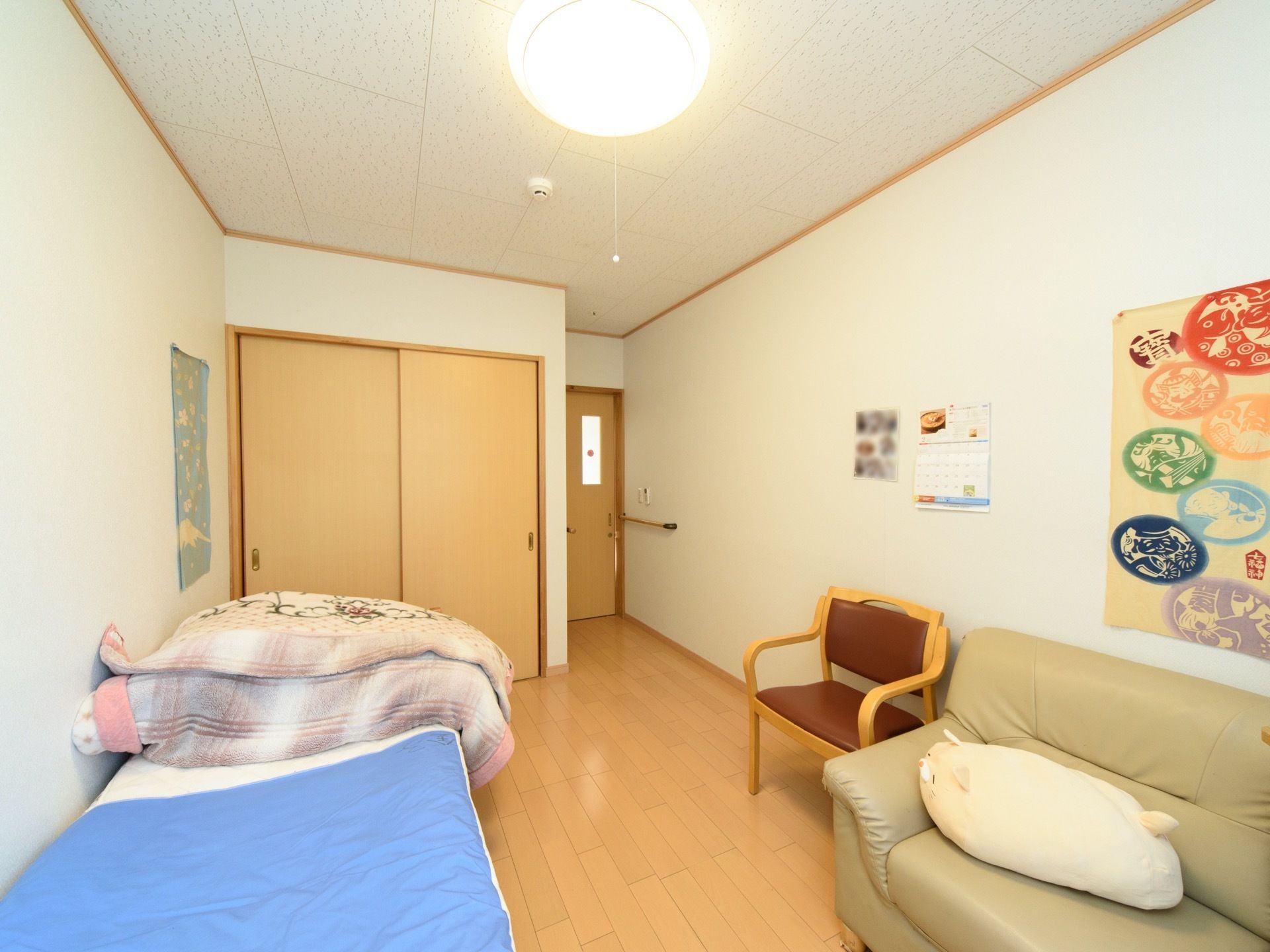 木調建具を使用した家庭的な雰囲気の洋式居室である。家具として、ベッドのほかに椅子やソファが置かれている。