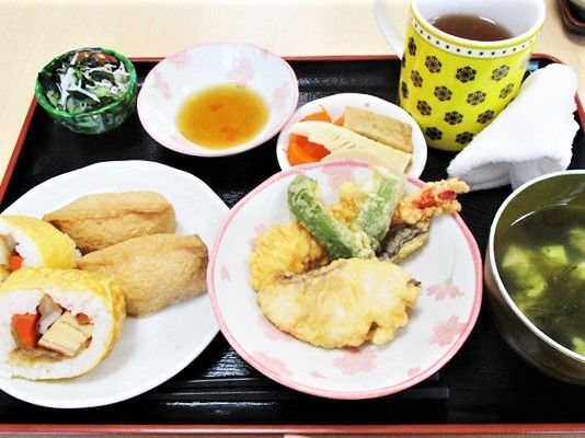 黒いトレーに並べられた食事。稲荷寿司や巻き寿司に汁物、天ぷらに煮物など豪華な内容。