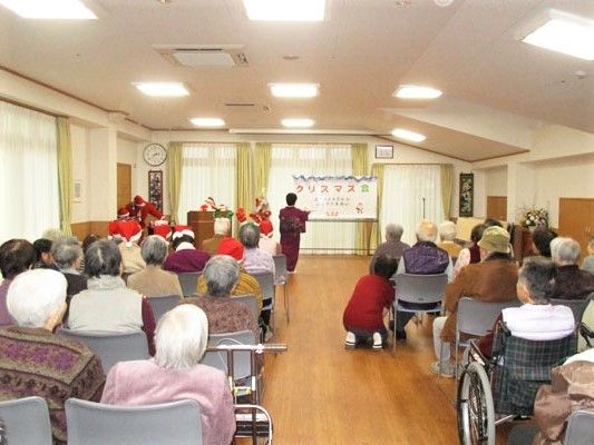 正面をステージに見立てて椅子が並べられ、着物を着た女性の踊りを見物している入居者たち。
