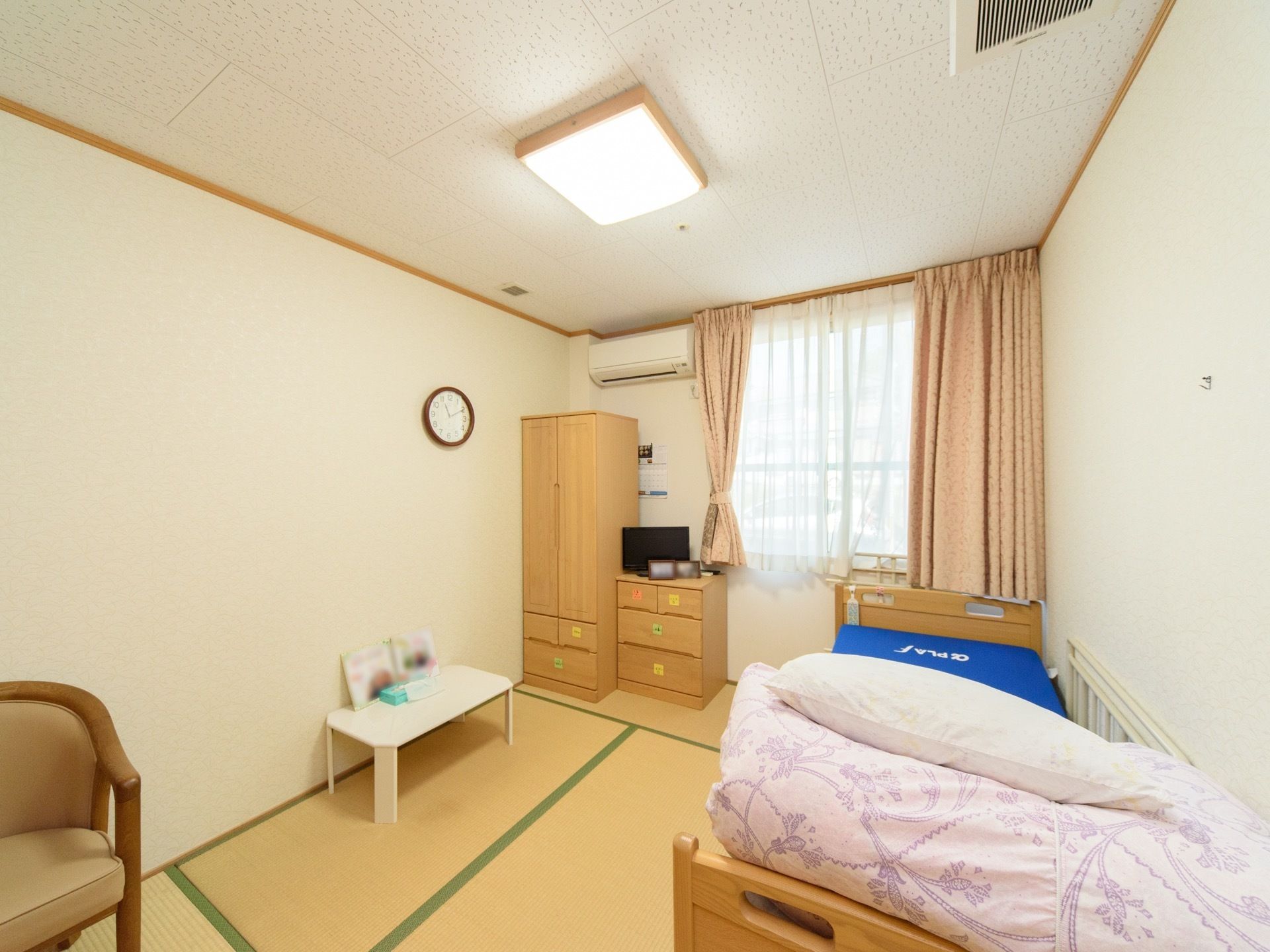 エアコンが完備された和室である。大きな窓から日光が差し込む明るい室内だ。衣類の収納に使える収納ボックスやタンスが配置されている。