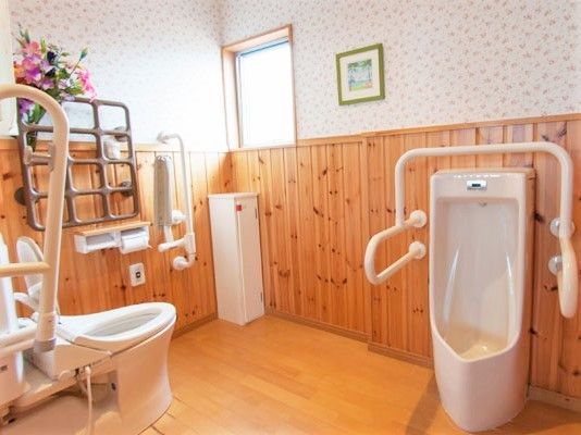明るい雰囲気のトイレは木目調と花柄の壁紙が印象的。数多くの手すりが付き、男性用小便器と洋式トイレがある。