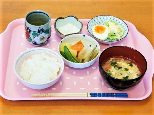 ピンクのトレーに並べられた食事。白いご飯に汁物、メインの煮物にサラダなど。