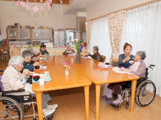 車いすの入居者も一緒にテーブルにつき、食事を食べている。数名のスタッフが介助に当たっている。