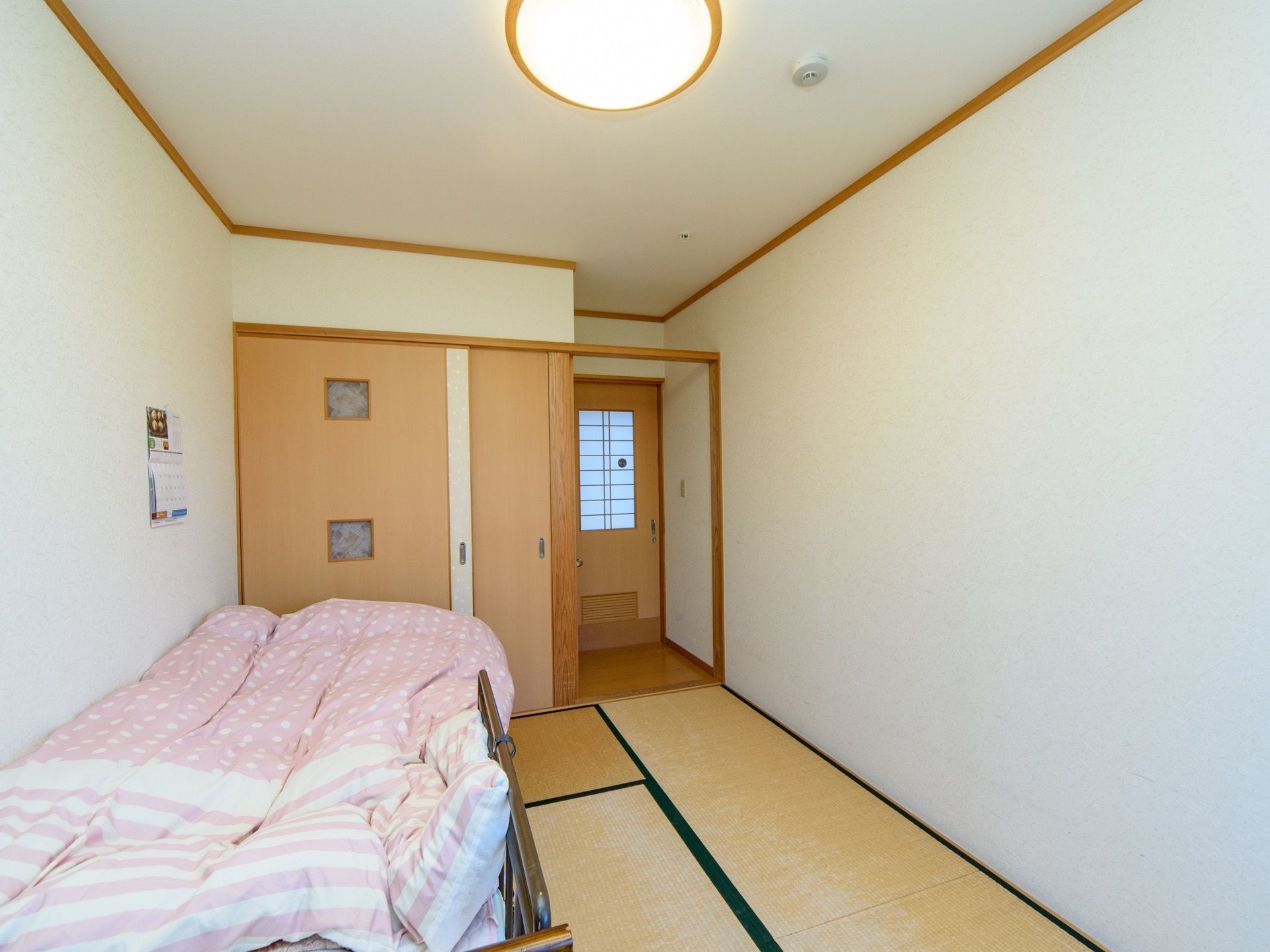 居室は和室タイプで段差がない。介護ベッドが完備されており、壁にはカレンダーが掛けられている。白を貴重とした広々とした空間である。