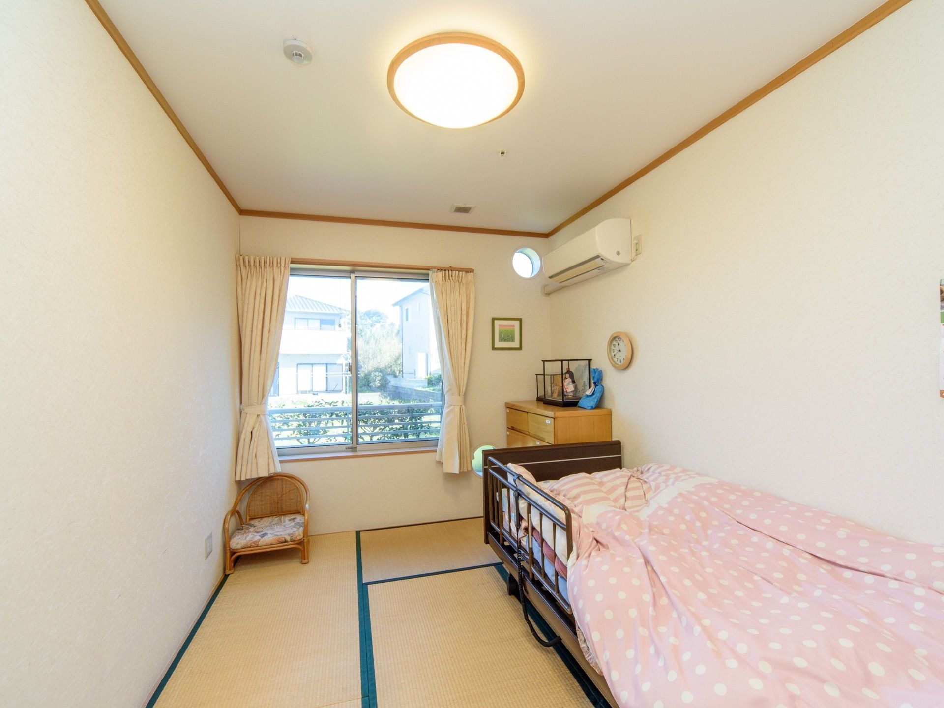 エアコンが完備されている居室。大きな窓からは外の景色を眺めることができる。箪笥の上には人形や小物が飾られている。