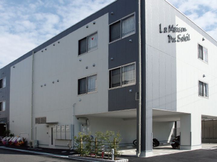 白を基調とした3階建ての建物の外壁にはホーム名が書かれていて、1階部分には駐車スペースもある。