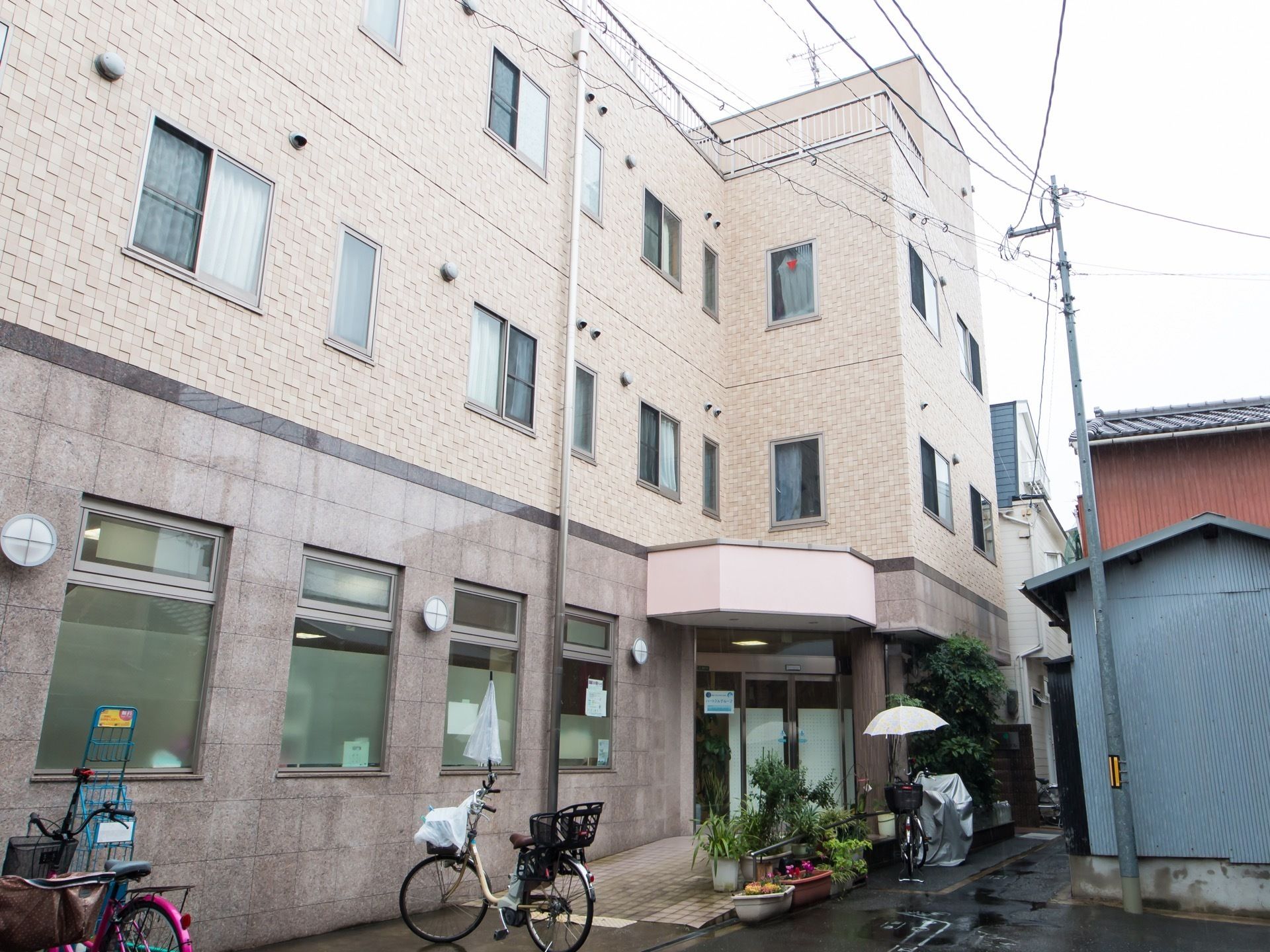 アスファルトで舗装された敷地に施設が建っている。玄関の前に鉢植えが並んでおり、建物の周囲に複数の自転車が停めてある。