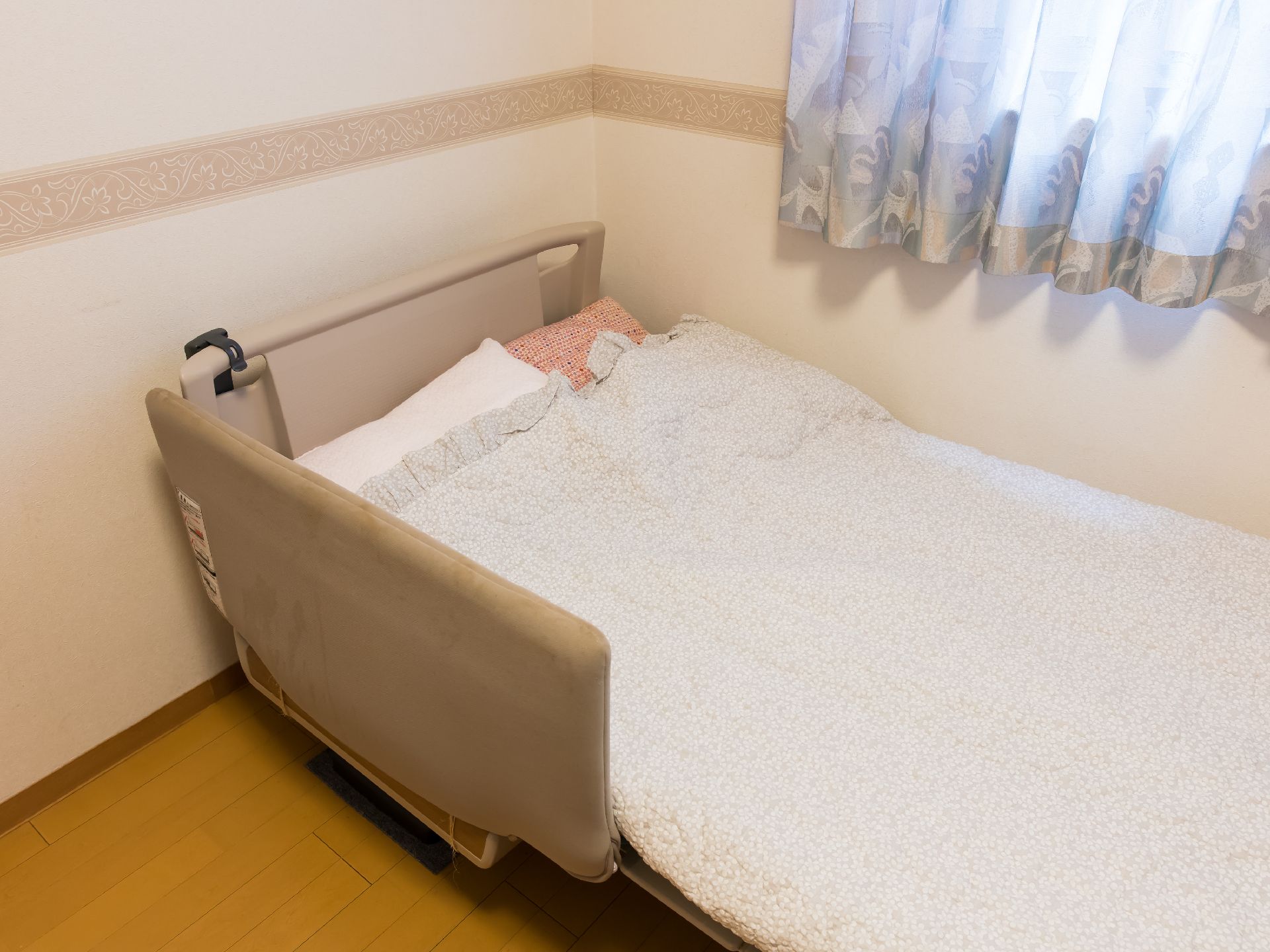 窓際に配置された寝具が整えられている電動介護ベッド