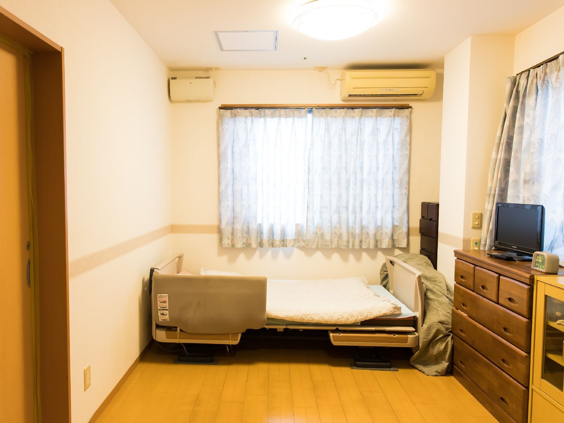 エアコンが完備されており、窓際に電動介護ベッドや収納家具を配置した居室