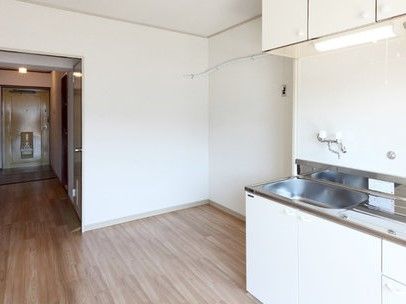 白い壁に白いキッチン、ブラウン系のフローリングというシンプルな居室。家具などは置かれていない。