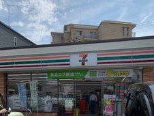 のぼりがいくつか立っているセブンイレブンの店舗。駐車スペースには車が数台止まっている。