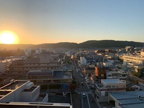 周辺には建物が多くにぎやかな雰囲気。朝が明け始めたばかりだが、道路には車が走っている。