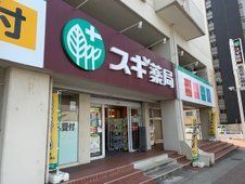 緑色の縁の中に葉のイラストが描かれ、その横に「スギ薬局」と書かれている。建物の1階部分にあるドラッグストア。
