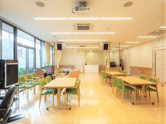 カラオケ機器やテレビ、大きな木製のダイニングテーブルセットが複数置かれたスペース。大きな窓も付いている。