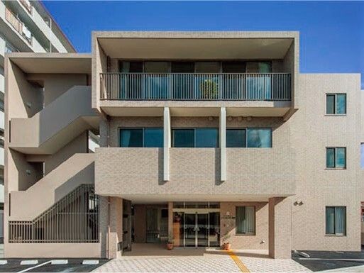 3階建ての建物はブラウン系で玄関には車寄せが付き、段差もない。点字ブロックが敷かれ、駐車場もすぐそばにある。