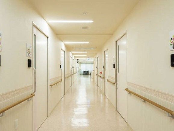 木製の手すりが両サイドに設置された白を基調とした館内。廊下の両サイドに居室のドアが並んでいる。