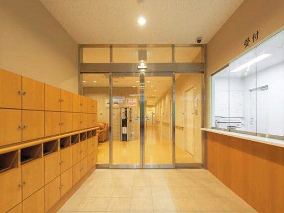 右側には受付、左側には靴箱があり、正面の自動ドアの向こうには手すりが付いた廊下やドリンクサーバーが見える。