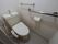 温水洗浄便座が設置されたトイレが中央にある。壁にはステンレス製の手すりやトイレットペーパー、タオル掛けが取り付けられている。