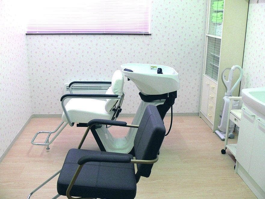 白と黒の専用のいすが設置された理美容室。洗面所や棚があり、花柄の壁紙も雰囲気を出している。