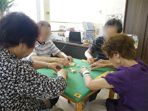 麻雀をしている女性の入居者４人。それぞれ手を麻雀卓の上に置き、真剣な勝負が繰り広げられている。