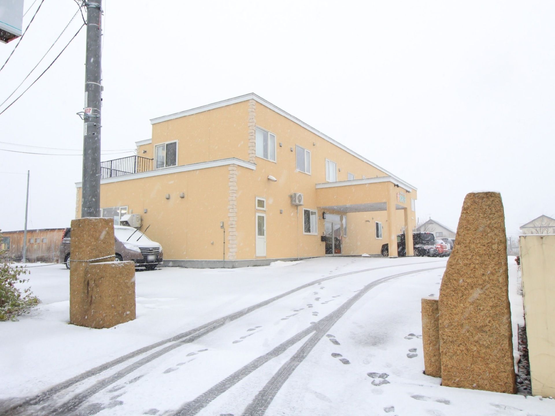 クリーム色の２階建て施設が広々とした敷地に建っている。車寄せがエントランス部分に設けられており、駐車場が建物前に用意されている。