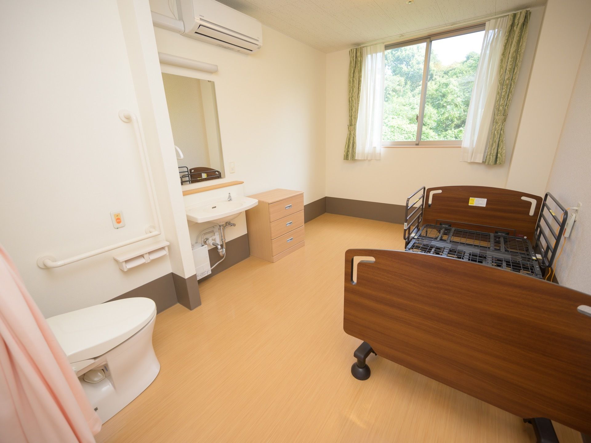居室はワンルームタイプである。介護ベッドやトイレ、洗面台が備わっており、壁にエアコンがある。
