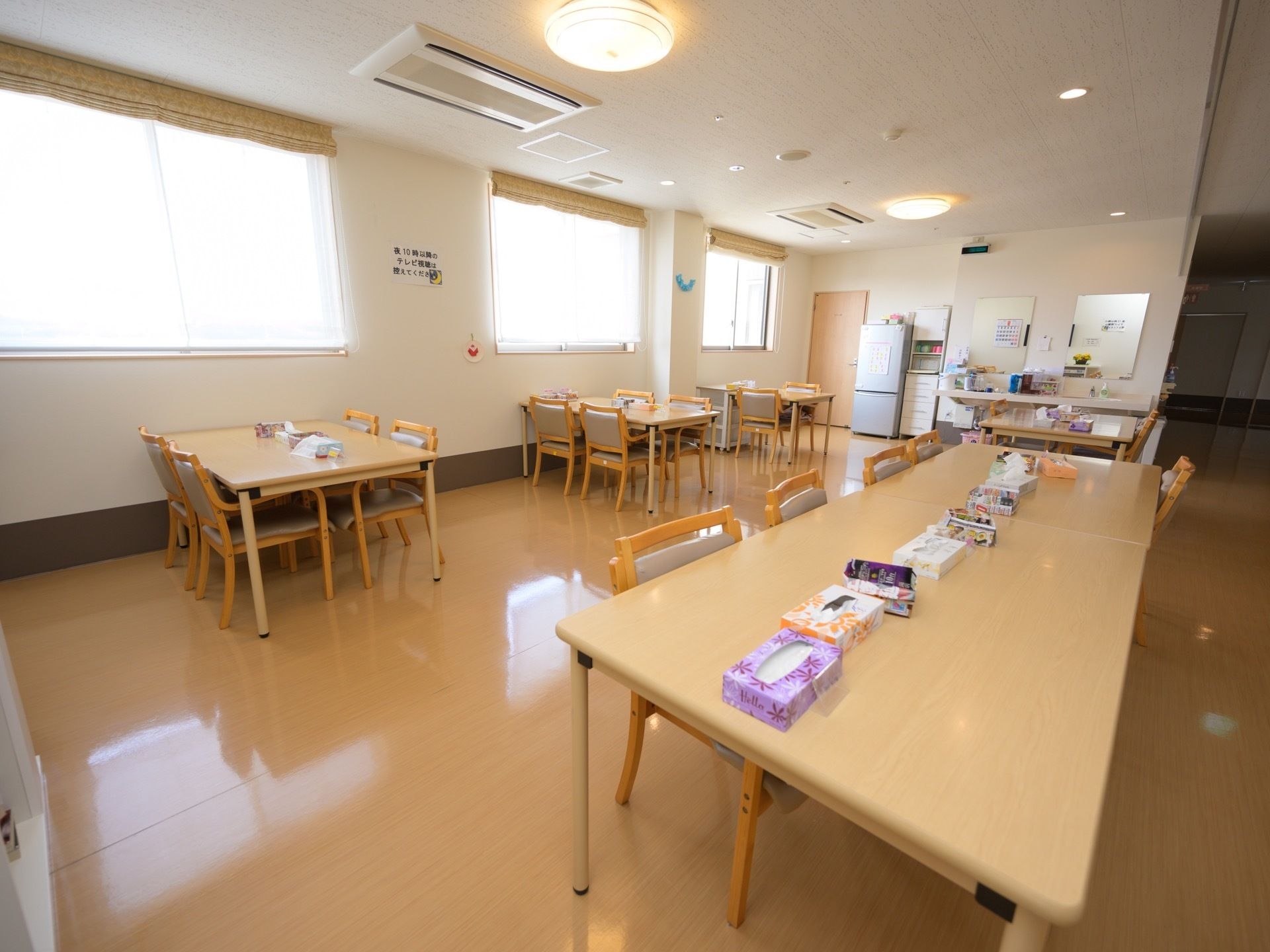 食堂は各居住フロアのホールに設けられている。複数の４人掛けテーブルが配置されている。右奥の壁際には、冷蔵庫が置かれている。