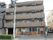 4階建てのマンション風の外観の建物である。各階にベランダ、エアコンの室外機が見える。周囲は市街地である。左側にエントランスがある。