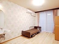 介護ベッドやエアコン、洗面所が付いたフローリングの部屋には大きな窓があり、収納家具も置かれている。