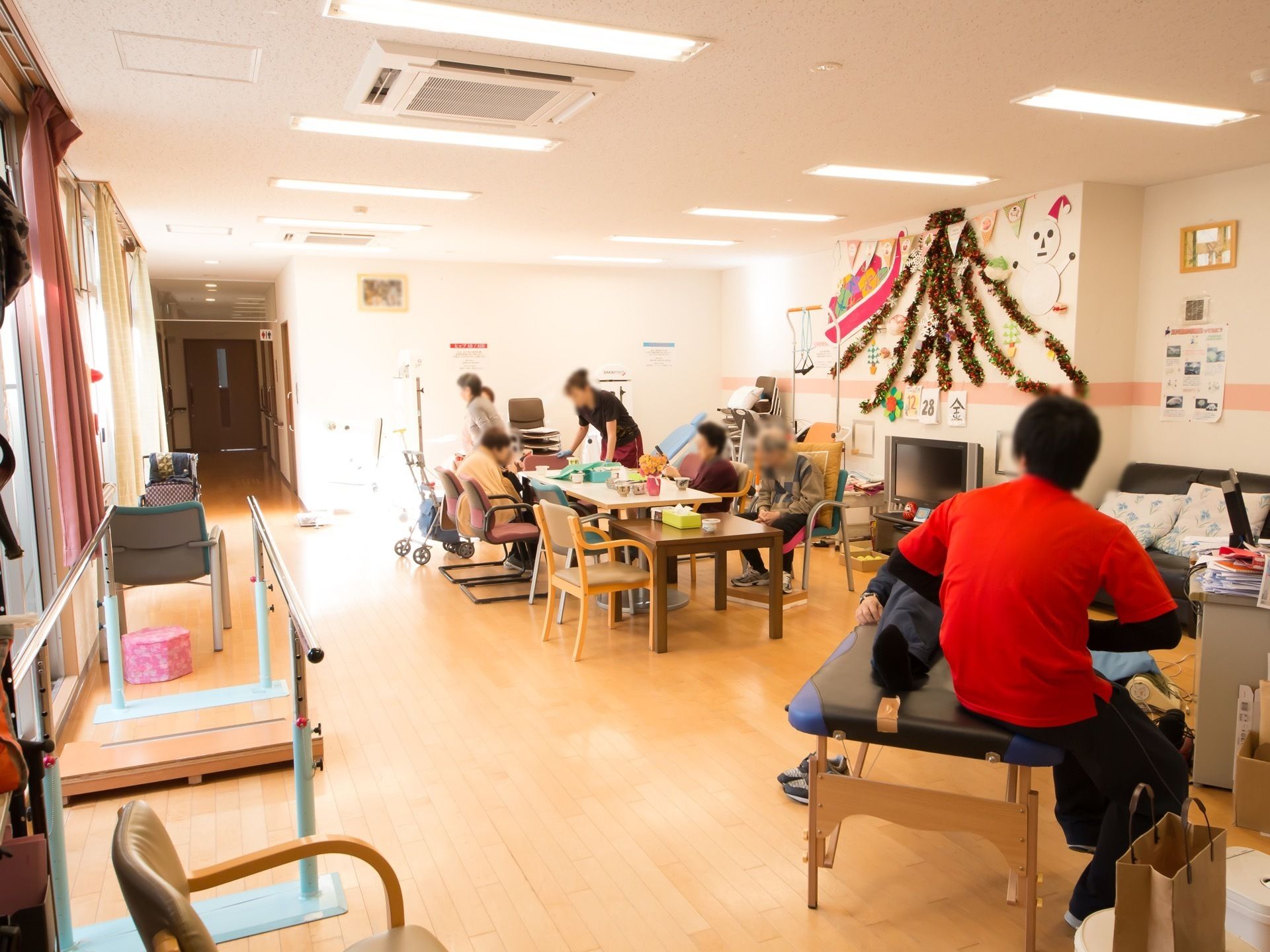 共有スペースに入居者様が集まっている。テーブルには女性スタッフがいる。男性スタッフがマッサージをしている。
