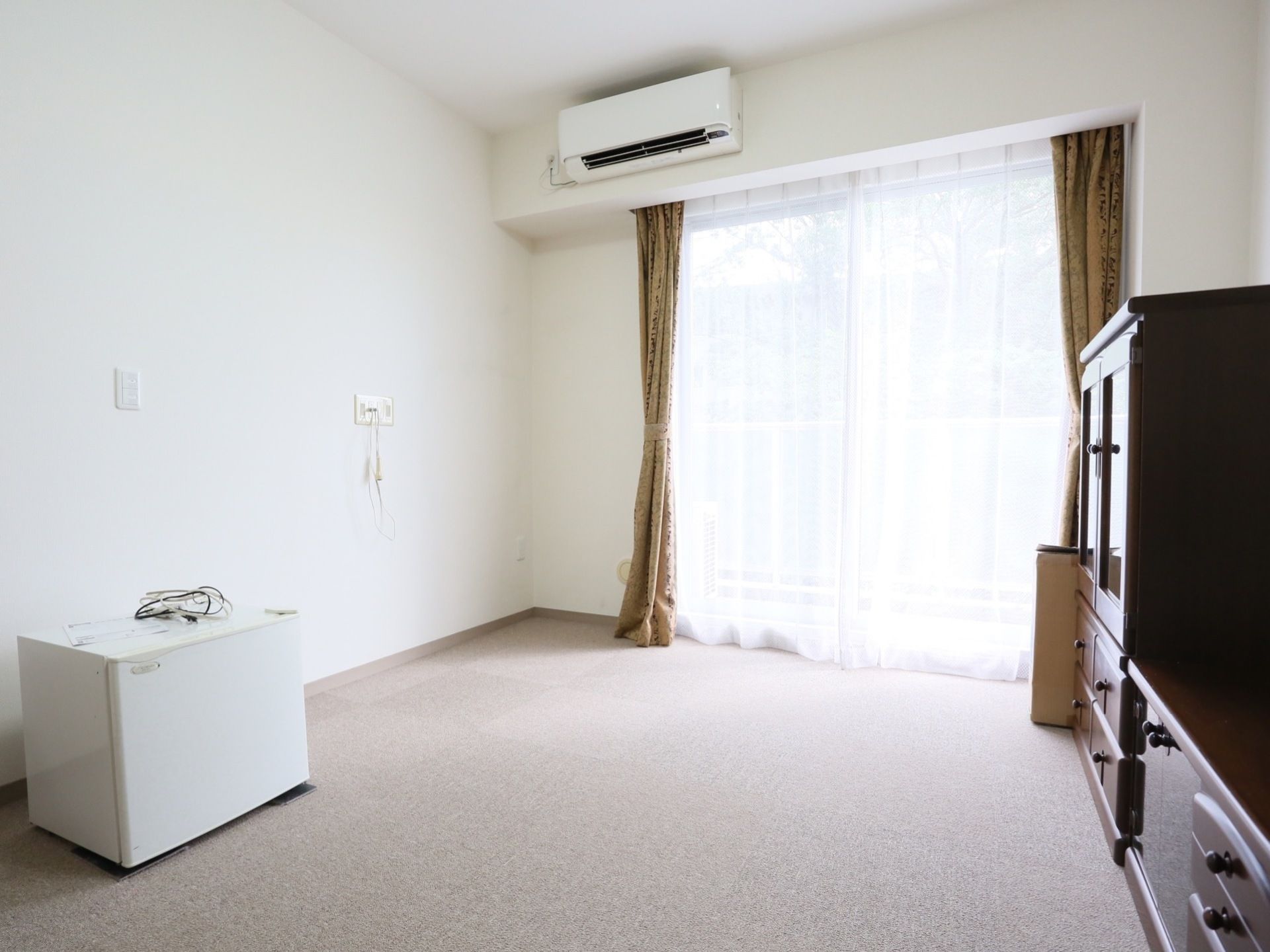 白を基調とした明るい空間になっており、壁にはナースコールが備えてある。大きな窓にはレースカーテンと、ベージュのカーテンが掛けられている。