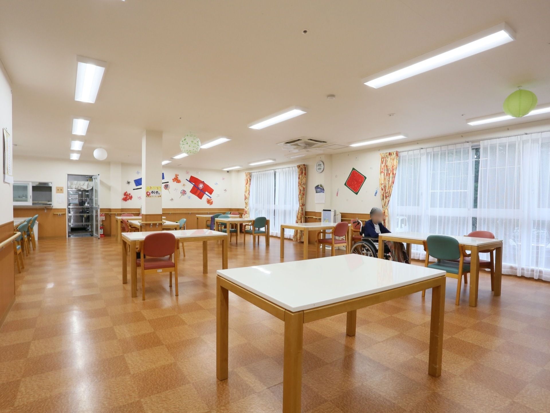 床は茶色の格子柄になっており、掃除が行き届いてきれいである。窓にはレースカーテンが引かれており、花柄のカーテンが束ねられている。