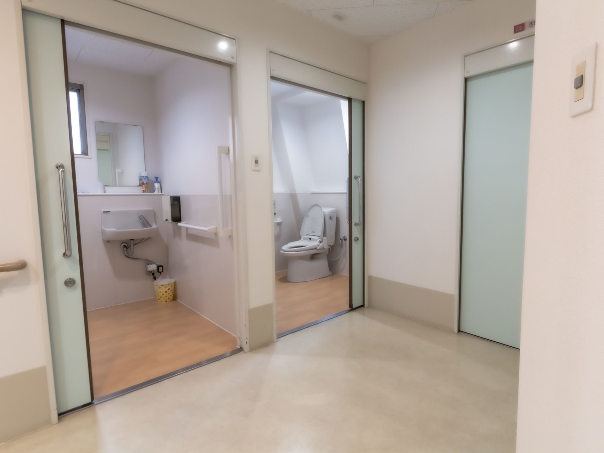 トイレの内部は広々としている。独立した洗面台が設置されており、自動水栓である。扉は大きくスライド式になっている。
