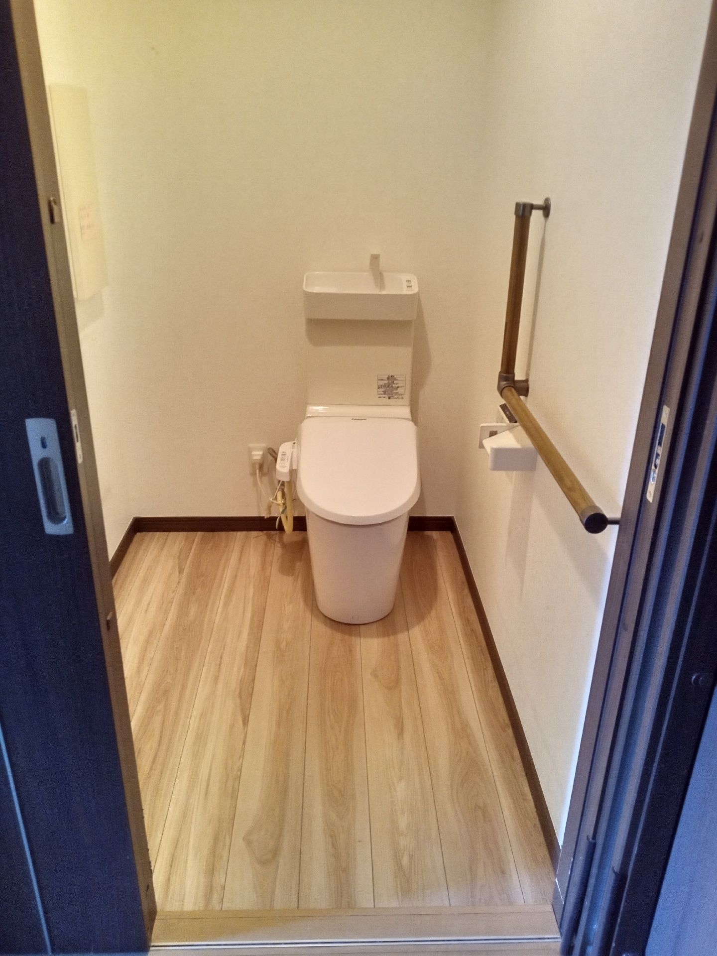 引き戸が設置されたトイレ内は広く、壁には手すりと手トイレットペーパーホルダーがある。