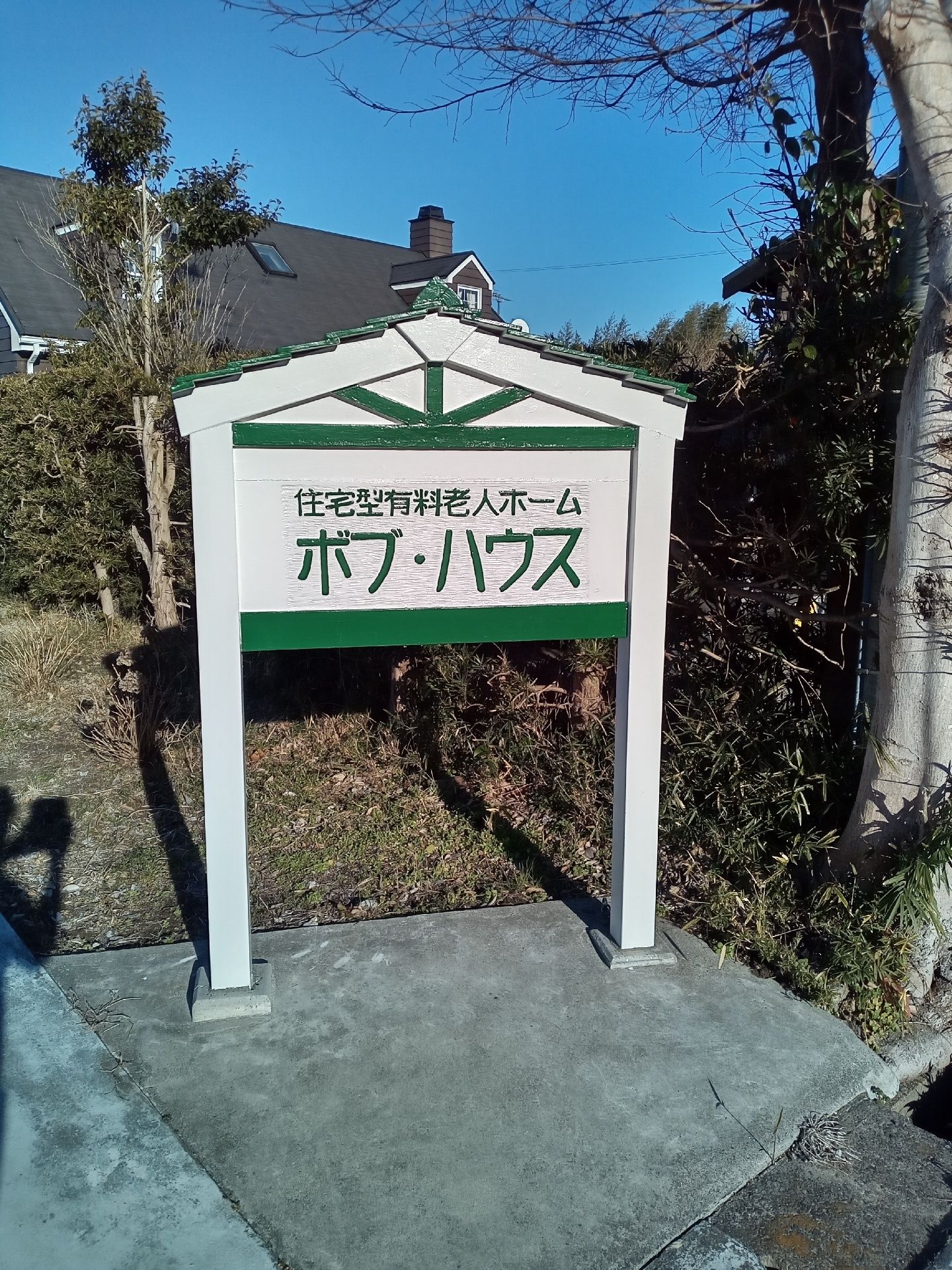 住宅名がグリーンの文字で書かれた白い看板が建てられている。看板は家の形をしている。