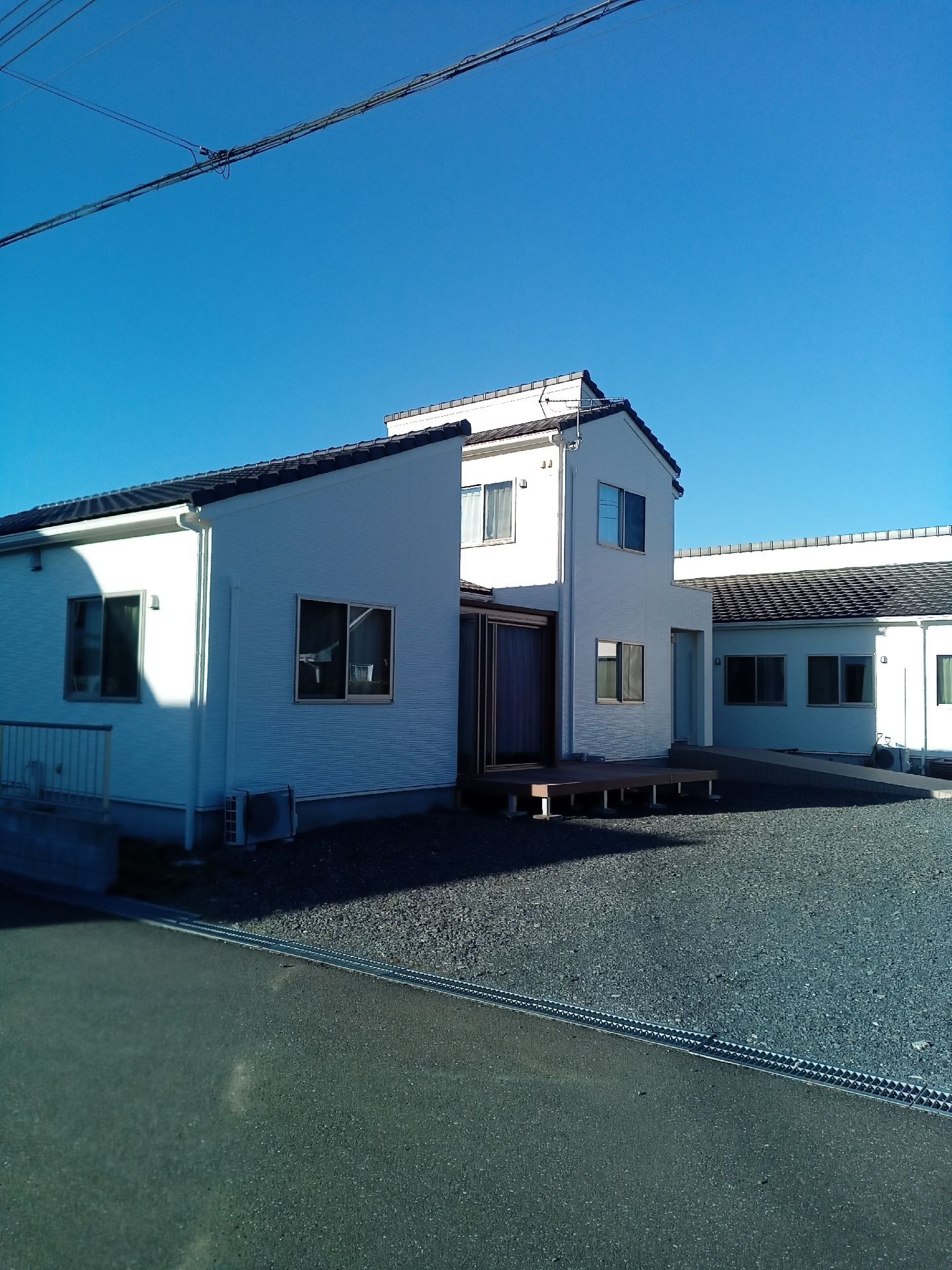 日当たりのいい場所に建っている一部平屋建ての2階建ての建物。白を基調にしていて窓が多い。