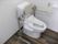 トイレを斜めから見た様子。可動式の手すりが両サイドにつき、背もたれもある。