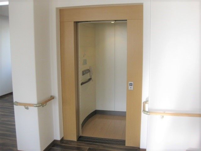 エレベーターは木目調の枠で囲まれナチュラルな雰囲気。手すりもすぐ際まで設置されている。